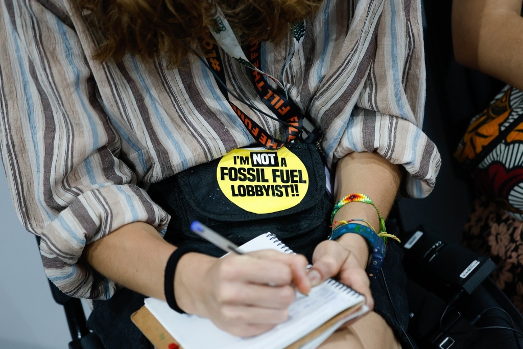 A COP30 participant wears a badge reading 'I'm not a fossil fuel lobbyist!!'