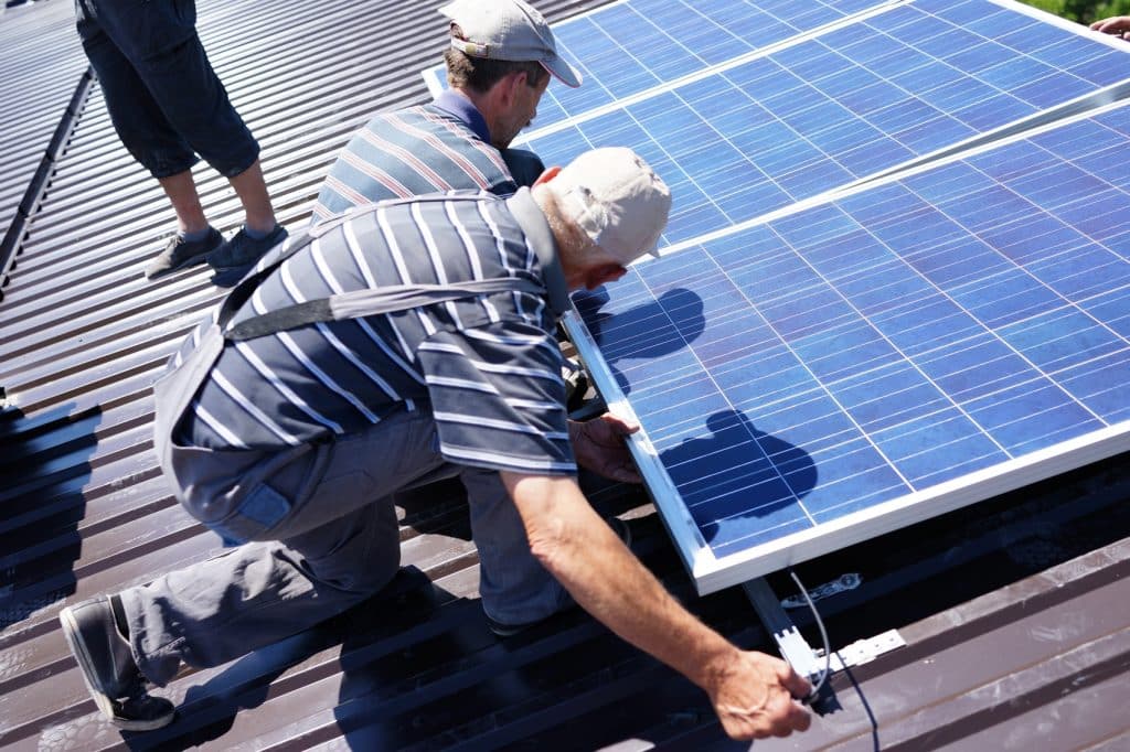 Workers installing alternative energy photovoltaic solar panels on roof.