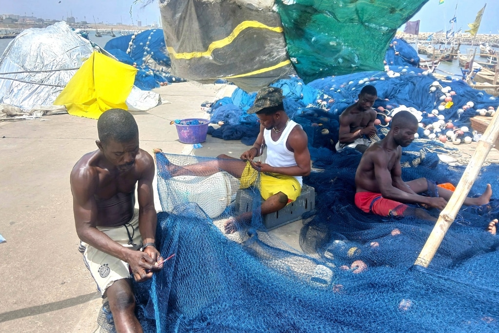 Fisherman Okai Addo and his colleagues sit in the sun to repair fishing nets as temperatures hit 31C.